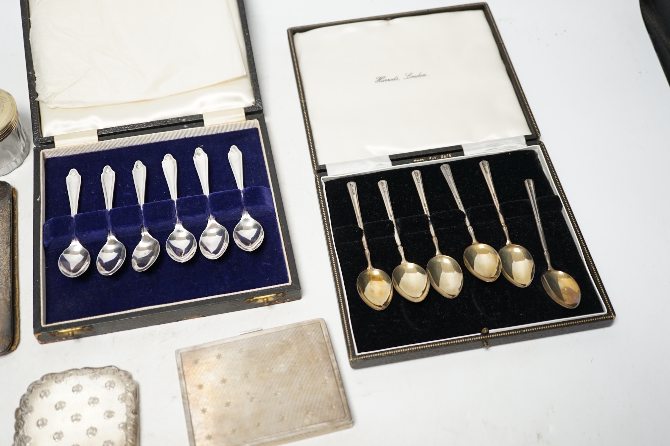 Two cased sets of six silver coffee spoons, a silver mounted leather case, two white metal cigarette cases, a white metal compact and a toilet jar. Condition - poor to fair